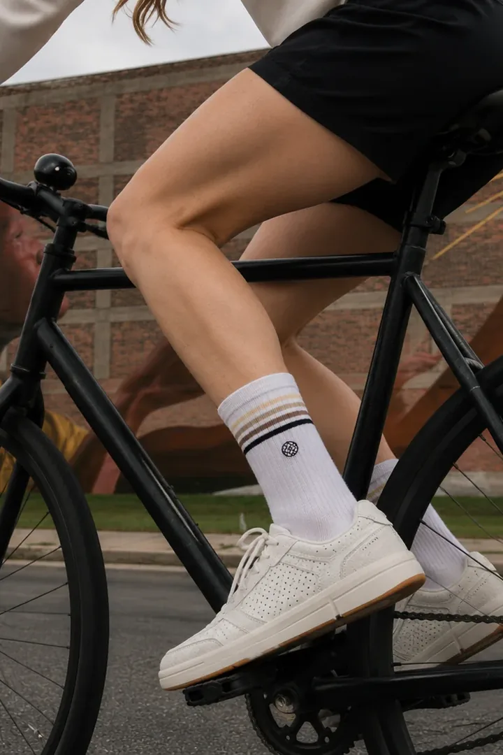 A cyclist wearing Unity Road striped white crew socks and cream trainers, riding past a brick wall